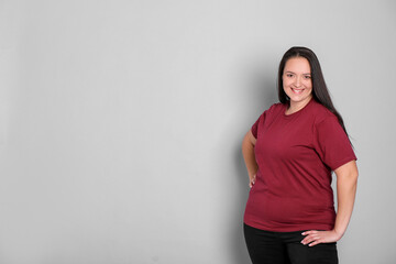 Beautiful overweight woman with charming smile on light grey background. Space for text - obrazy, fototapety, plakaty