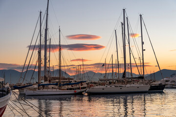 Fototapeta na wymiar Sailboats, fishing boats and yachts reflect off the sea at sunset in the small fishing village of Aegina, on the island of Aegina, Greece. 