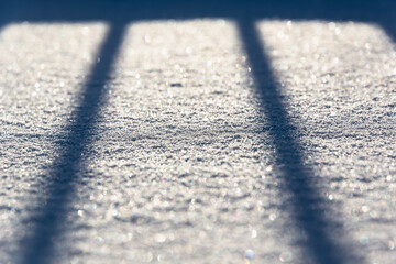 Shadows on the snow from the fence.