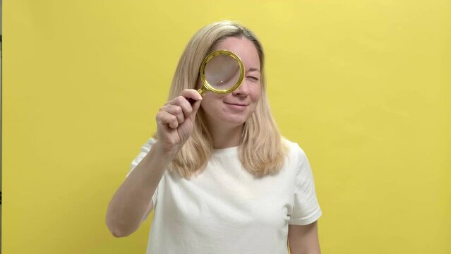 4k. Young smiling woman in a white T-shirt examining details through magnifying glass, learning ins and outs. Close up of young blond girl looking through magnifying glass