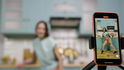 Focus on phone screen with young girl dancing and making videos for their blogs or social networks. Blogger are recording vlog with trend content in kitchen. Slow motion ready, 4K at 59.97fps.