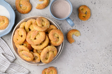 Naklejka premium Sugar pretzels in a plate for breakfast. Cottage cheese cookies with mug of cocoa . Healthy dessert. Top view. Copy space
