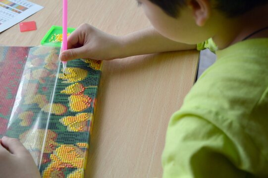 The child is engaged in creativity, lays out diamond embroidery, a picture of beads.