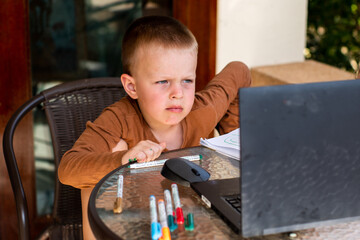 A little boy is looking at a laptop monitor. distance learning. children using technology. Children at the computer. Online training. Kids and gadgets. Doing his homework. Learning to draw. crafting, 