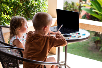 A little boy and a girl are sitting in front of a laptop. distance learning. children using technology. Children at the computer. Online training. Kids and gadgets. Siblings watch cartoons.