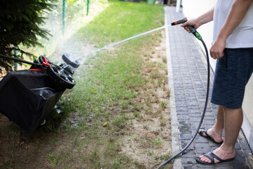 A man washes a lawn mower with a stream of water.