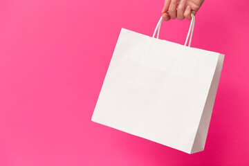 Female hand holding white blank shopping bag isolated on pink background. Black friday sale,...