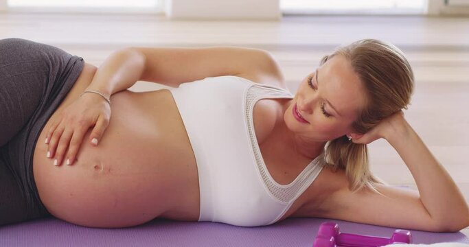 Baby enjoyed that one. Pregnant woman touching her belly while resting from exercising alone at home. Happy expectant mom doing workout, training and yoga to stay active, healthy and fit 