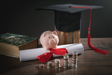 Graduation hat, book, diploma, coins and piggy bank on the wooden table.