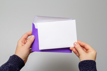 POV photo of a woman's hands in a blue sweater holding an open envelope with a white card on an isolated white background with empty space