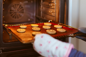 Detail of person putting a tray of cookies in the oven. Close up. Cropped image.