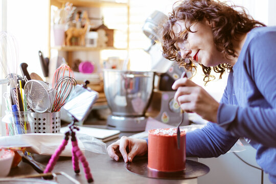 Young woman at home teaching an online baking class. She is using a mobile phone on a tripod. Food blogging.
