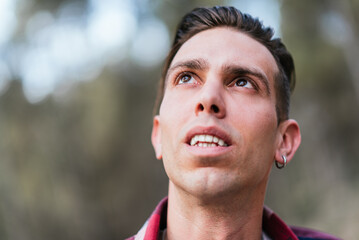Serious male with ear piercing looking up with interest while spending day in nature