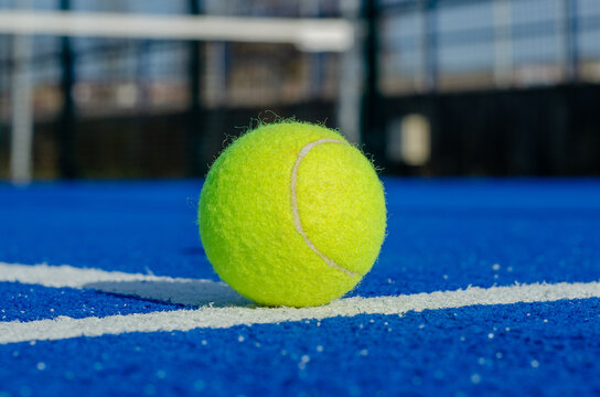 Ground level image of a ball on a blue paddle tennis court lines