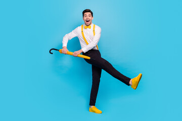 Full body of excited carefree guy enjoy discotheque 60s hold yellow umbrella isolated on blue color background
