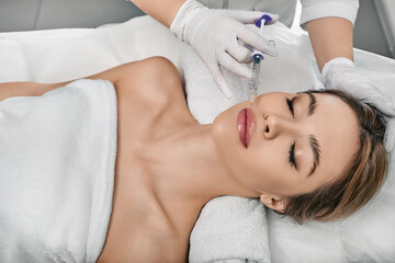 Obraz na płótnie Canvas Female patient during lip augmentation procedure at beauty clinic with cosmetologist. Filler injection for beautiful female lips augmentation with hyaluronic