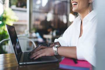 Cropped view of cheerful Caucasian female digital nomad laughing at table on cafe terrace, joyful...