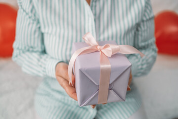 Happy Valentine day. Cropped photo of female hands holding small gift wrapped with pink ribbon indoors. Holiday web banner