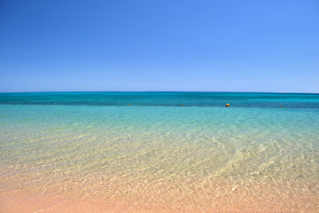 Seascape with surface of blue sea water with small ripple waves crashing on yellow sandy beach. Travel and vacations concept