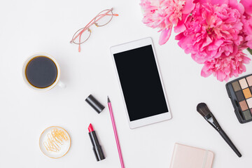 Obraz na płótnie Canvas Flat lay concept online shopping cosmetics. Smartphone with blank screen mockup, notepad, glasses, cup of coffee and pink peonies on a white table.