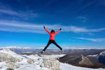 Woman hiker in the mountains jumps happy in the blue sky