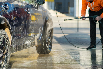 Young driver man washing his car with contactless high pressure water jet in self service car wash