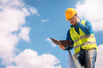 young caucasian engineer man leaning on a railing, talking and planning on the phone with the sky in the background and copy space.