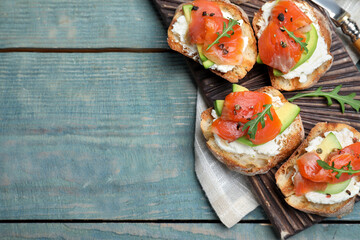 Delicious sandwiches with cream cheese, salmon, avocado and arugula served on light blue wooden table, flat lay. Space for text
