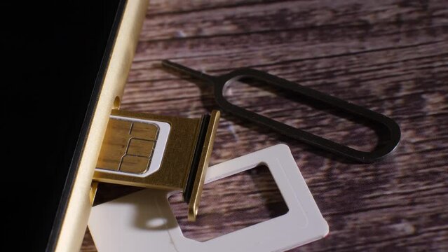 Closeup shot of the sim card slot of a smartphone. Showing the tool needed to open it. Modern technology. Communication. Wood background. Golden colored phone. Camera slowly moving around.