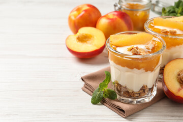 Tasty peach yogurt with granola, pieces of fruit and jam on white wooden table, space for text