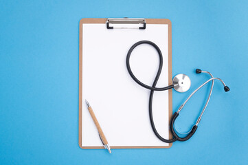 Top view, medical accessories on blue background. Wooden notepad, black stethoscope, white pen. Flat lay, mockup