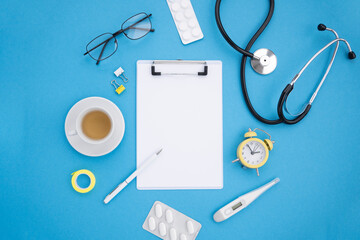 Top view Medical desk. Stethoscope, thermometer, pills, medicines, glasses, coffee cup, watch, on a blue background. Flat lay, mockup