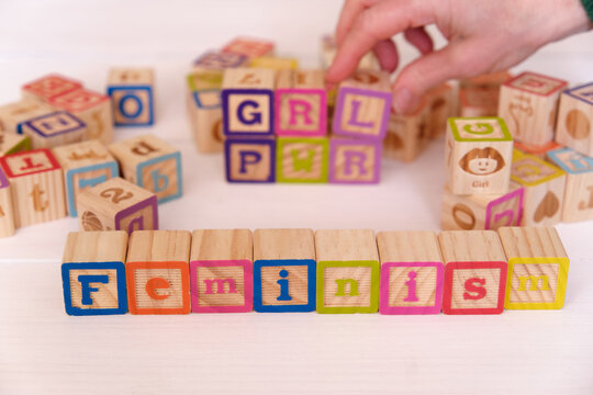 A woman writing the word feminism and the initials GRL PWR with blocks of wooden cubes.