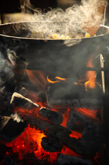 Food is fried in pan over open fire in the grill. The process of cooking over fire. Vertical photo of food. Smoke over food on fire against the background of the forest.