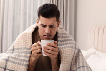 Sick man with cup of hot drink on bed at home