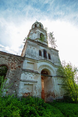 Fototapeta na wymiar Side view of the courtyard facade of the bell tower of an old, destroyed and abandoned church in Russia. Walls with peeling paint and old red bricks. Trees on the roofs. Summer. Daylight.