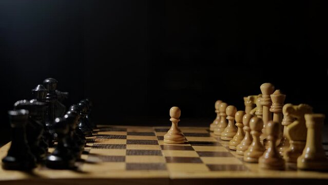 A man hand with a chess piece in a board game. Opening of the chess game with the move of the white king pawn e2-e4, copy space on a black background