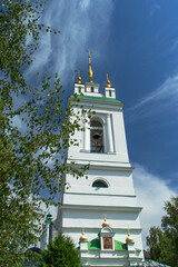Russia, Vladimir region, Konstantinovo village: Front view of the white bell tower of the Orthodox Church against the blue sky. In the foreground - the crowns of green trees. Daylight.