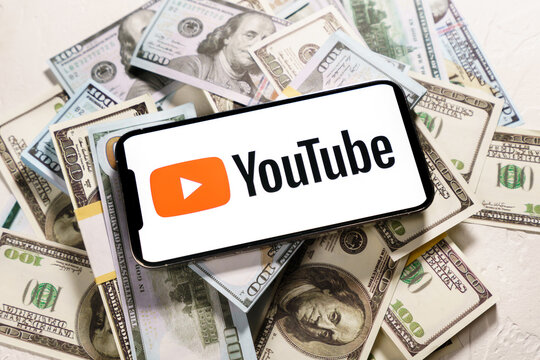 Berlin, Germany - February 02, 2022: Dollars banknotes and YouTube logo on the screen  iPhone 12 Pro Max. YouTube is a free video sharing application that