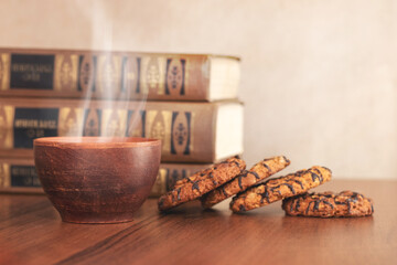 Cup with hot tea or coffee and cookies near books in the library. Food while studying