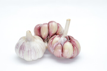 Three heads of garlic (Allium sativum), with one still unpeeled and the other two lightly peeled, each clove can be seen in rosy tones on the edges and on a neutral background