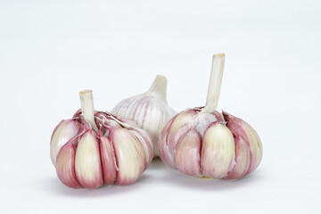 Three heads of garlic (Allium sativum), with one still unpeeled and the other two lightly peeled, each clove can be seen in rosy tones on the edges and on a neutral background