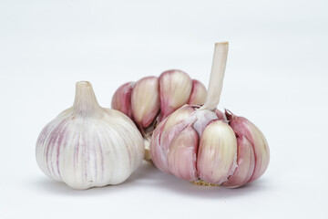 Three heads of garlic (Allium sativum), with one still unpeeled and the other two lightly peeled, each clove can be seen in rosy tones on the edges and on a neutral background