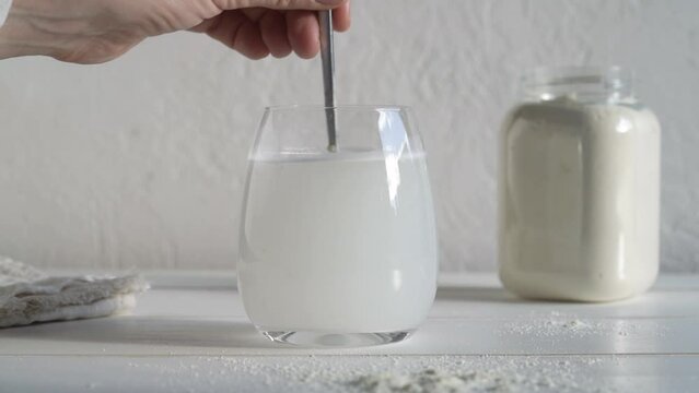 Stirring whey protein powder in a glass of water on white background, slow motion