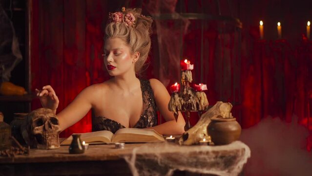 Fortune teller woman reading future magical necromancer book. Magic and divination. Beautiful enchanted female witch sitting on the table touching human skull. Scary Halloween atmosphere Handheld 