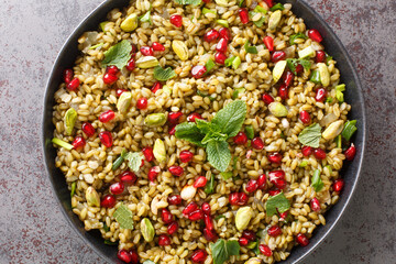 Healthy vegan food made of freekeh with pomegranate, nuts and herbs close-up in a plate on the...