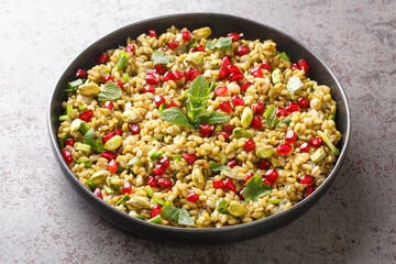 Delicious vegetarian freekeh with pomegranate, nuts and herbs close-up in a plate on the table. horizontal