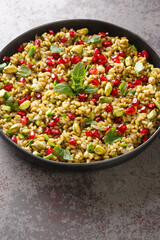 Vegetarian salad with freekeh, pomegranate, nuts and herbs close-up in a plate on the table. Vertical