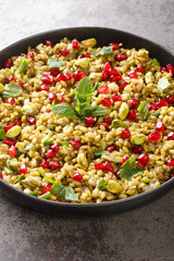 Freekeh salad with pomegranate seeds, pistachios, mint and spring onion close-up in a plate on the table. Vertical