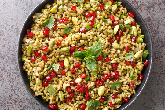 Healthy vegan food made of freekeh with pomegranate, nuts and herbs close-up in a plate on the table. horizontal top view from above